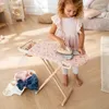 A young girl is playing with a toy ironing board and iron. Podgląd zdjęcia produktu