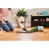 A person is using a handheld vacuum cleaner to clean up spilled dirt from a fallen plant on a wooden floor. Produktbild-Vorschau