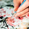 A person's hand is painting a picture using a paintbrush and small pots of paint. Produktbild-Vorschau