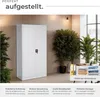 A white metal cabinet is shown in a room with plants and a desk in the background. Text overlays describe features. Produktbild-Vorschau