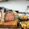 A prime rib roast is presented on a wooden cutting board with a thermometer inserted, accompanied by a salad and roasted potatoes. Náhled obrázku produktu