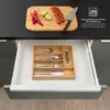 A kitchen drawer with a bamboo cutlery organizer filled with silverware and a corkscrew, with a cutting board with chilies, limes, and tomatoes visible above. Podgląd zdjęcia produktu