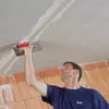 A man is applying plaster to a ceiling with a trowel. Produktbild-Vorschau