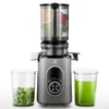 A slow juicer with a clear container of chopped vegetables on the left and a glass of green juice on the right. Produktbild-Vorschau