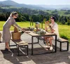 A couple enjoying a meal at a picnic table set up on a wooden deck with a scenic view of rolling hills and greenery. Produktbild-Vorschau