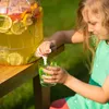 A young girl is pouring lemonade from a large dispenser into a glass. Produktbild-Vorschau