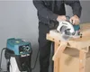 A person is using a Makita circular saw connected to a Makita vacuum cleaner to cut a piece of wood on a workbench. Produktbild-Vorschau