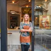 A woman stands in the doorway of a coffee shop, smiling. Náhled obrázku produktu