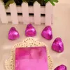 Heart-shaped chocolates wrapped in pink foil are arranged on a white doily in front of a white picket fence. Produktbild-Vorschau