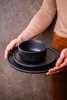 A person holding a stack of black plates and a bowl. Náhľad obrázku produktu