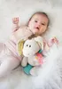 A baby lying on a white fluffy surface with a stuffed donkey toy. Podgląd zdjęcia produktu