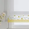 A close-up view of a window with a roman blind featuring a floral embroidery pattern and a yellow band. Produktbild-Vorschau