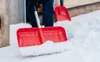 A person is shoveling snow with a red snow shovel. Náhled obrázku produktu