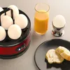 A close-up of an egg cooker with eggs, a glass of orange juice, and bread on a plate. Anteprima dell’immagine prodotto