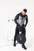 A man in athletic wear is holding a weight plate attached to a chain, standing next to a pull-up bar. Náhľad obrázku produktu