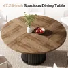 A round dining table with a wood-grain top and a fluted black base, set in a dining room with chairs. Produktbild-Vorschau