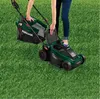 A person is using a green and black electric lawnmower on a grassy lawn. Produktbild-Vorschau