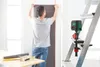 A person is hanging wallpaper while a laser measuring device is attached to a ladder. Produktbild-Vorschau