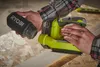 A person is holding a dust collector attachment for a Ryobi sander while also holding the sander itself, which is resting on a wooden surface. Podgląd zdjęcia produktu