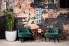 Two green velvet chairs are placed in front of a distressed brick wall, with a potted plant on the left and a small table with decorative items between the chairs. Anteprima dell’immagine prodotto