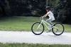 A young girl rides a white bicycle on a gravel path in a park. Produktbild-Vorschau