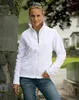 A woman stands outdoors in front of a stone wall and a building, wearing a white fleece jacket and jeans. Produktbild-Vorschau