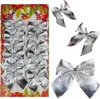 A set of 12 shiny silver Christmas tree bows arranged on a card with festive decorations. Náhľad obrázku produktu