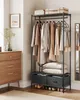 A SONGMICS open wardrobe with clothes hanging on it, two drawers at the bottom, and shoes on the lowest shelf. A dresser is visible to the left, and a mirror is partially visible to the right. Produktbild-Vorschau