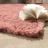 A close-up view of a fluffy pink rug with an open book resting on it. Produktbild-Vorschau