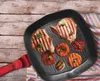 A grill pan with grilled pork chops and vegetables on a wooden table. Produktbild-Vorschau