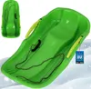 A green plastic sled with yellow handles and a rope, shown on a snowy background. Náhled obrázku produktu