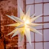 A lit-up star decoration hangs in front of a brick wall and a window. Produktbild-Vorschau