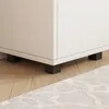 Close-up of the bottom of a white cabinet with black feet, resting on a wooden floor and partially over a rug. Produktbild-Vorschau