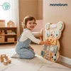A toddler plays with a wooden busy board in a nursery. Produktbild-Vorschau