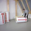 A person is handling insulation rolls in what appears to be an attic or unfinished room. Produktbild-Vorschau