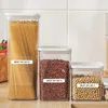 Three clear plastic food storage containers filled with spaghetti, red beans, and soybeans, arranged on a wooden surface against a tiled background. Each container has a white lid and a label indicating a 'BEST BY' date. Podgląd zdjęcia produktu