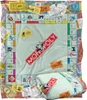 A collage of Monopoly game elements, including the board, money, and cards, with a folded blanket in the foreground. Produktbild-Vorschau