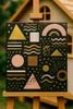 An abstract painting with geometric shapes and wavy lines on a black background, displayed on a wooden easel outdoors. Podgląd zdjęcia produktu