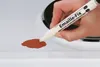 A hand is using a white marker pen to touch up a brown stain on a white surface, possibly a stovetop. Produktbild-Vorschau
