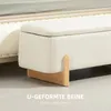 A close-up view of a cream-colored storage bench with wooden legs, placed next to a bed. Voir les images du produit