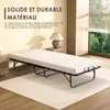 A folded bed with a mattress on it, placed on a rug in a room with a window overlooking trees. Voir les images du produit