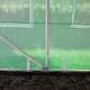 Close-up view of the bottom section of a greenhouse, showing the green transparent PE plastic sheeting and silver metal frame poles anchored into dark soil. Produktbild-Vorschau