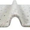 A close-up, angled view of a beige rug with black dots, showing its high pile texture and a rolled edge. Produktbild-Vorschau