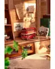 A miniature red double-decker bus is displayed on a wooden shelf, surrounded by vintage-style newspapers and books. Náhľad obrázku produktu