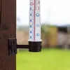 A thermometer is mounted on a wooden post outdoors, with a blurred green lawn in the background. Podgląd zdjęcia produktu
