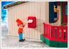 A toy elf figure is standing in front of a toy house, about to put a letter in a mailbox. Produktbild-Vorschau