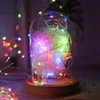 A close-up of a glass dome containing a string of colorful LED lights and white shredded paper, resting on a wooden base. Podgląd zdjęcia produktu