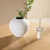 A white vase with green branches and a white candle in a holder on a wooden table. Voir les images du produit