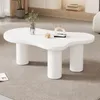 A white, irregular-shaped coffee table with three cylindrical legs sits on a grey carpet. Decorative items are placed on the table. Produktbild-Vorschau