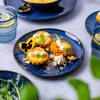A close-up of small tarts and a glass of water on a blue plate. Voir les images du produit